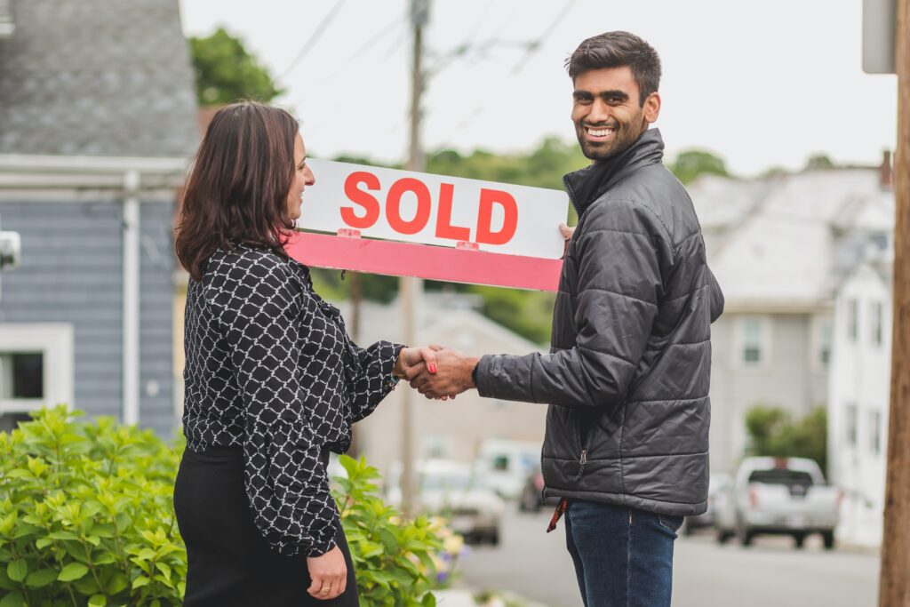 Want to Buy A House: A man and a lady is shaking hands. The man is holding a sold sign