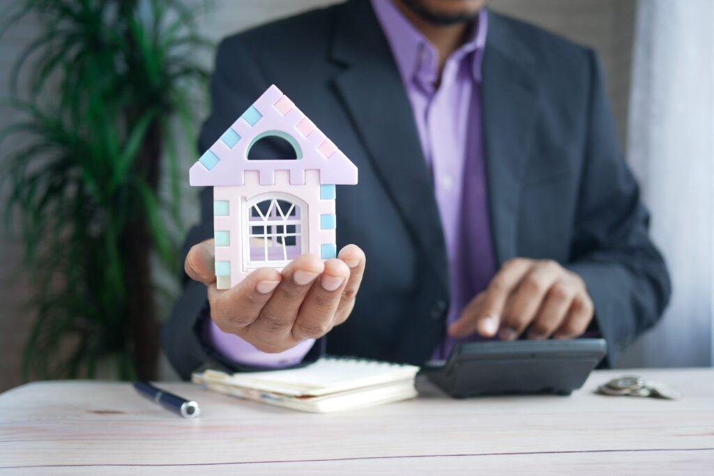 Pricing Your House: A miniature House is in the palm of a man while the other hand 's finger is pressing on a calculator